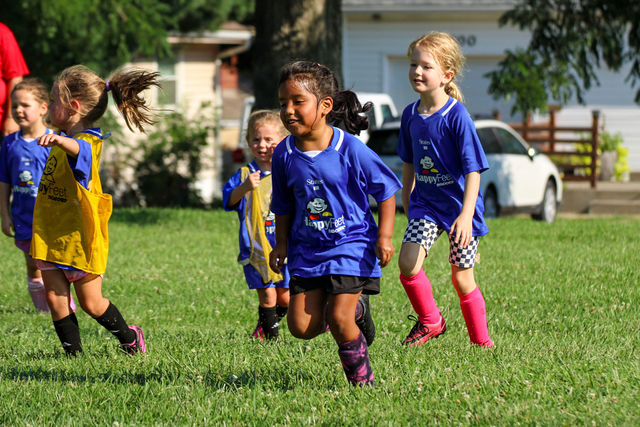 Girls in blue jerseys running and celebrating together at a HappyFeet soccer class