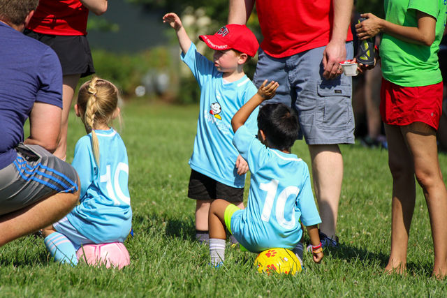 Young soccer player sitting on a ball pointing at HappyFeet