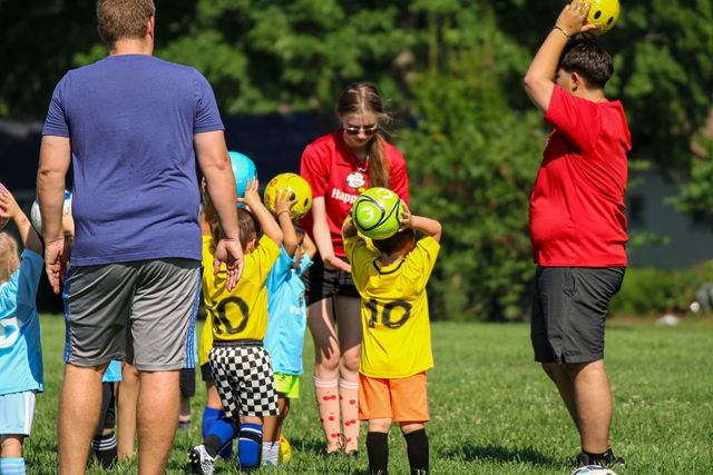 Players in mixed jerseys warming up with balls overhead at a HappyFeet class in Leawood, KS