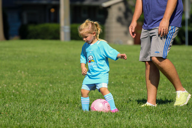 Toddler girl in light blue playing with a pink ball alongside a parent at a HappyFeet class in Roeland Park, KS