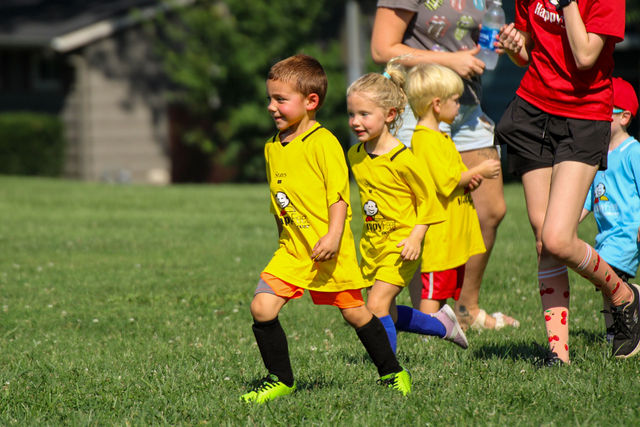 Two kids in yellow jerseys running with their coach at HappyFeet